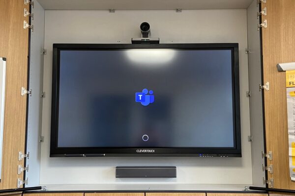 A wall-mounted clevertouch screen, part of the audio visual systems, displaying a blue and white logo inside a gray cabinet with open doors.