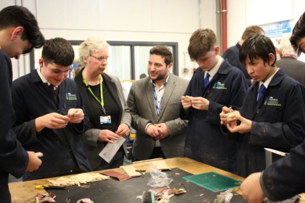 Group of students and instructors examining materials at a workshop table in a classroom setting.