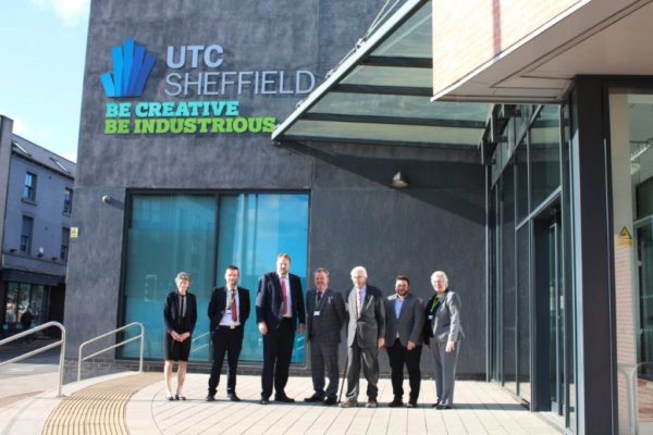 Seven professionals standing in front of the utc sheffield building, under a sign that reads "be creative be industrious.